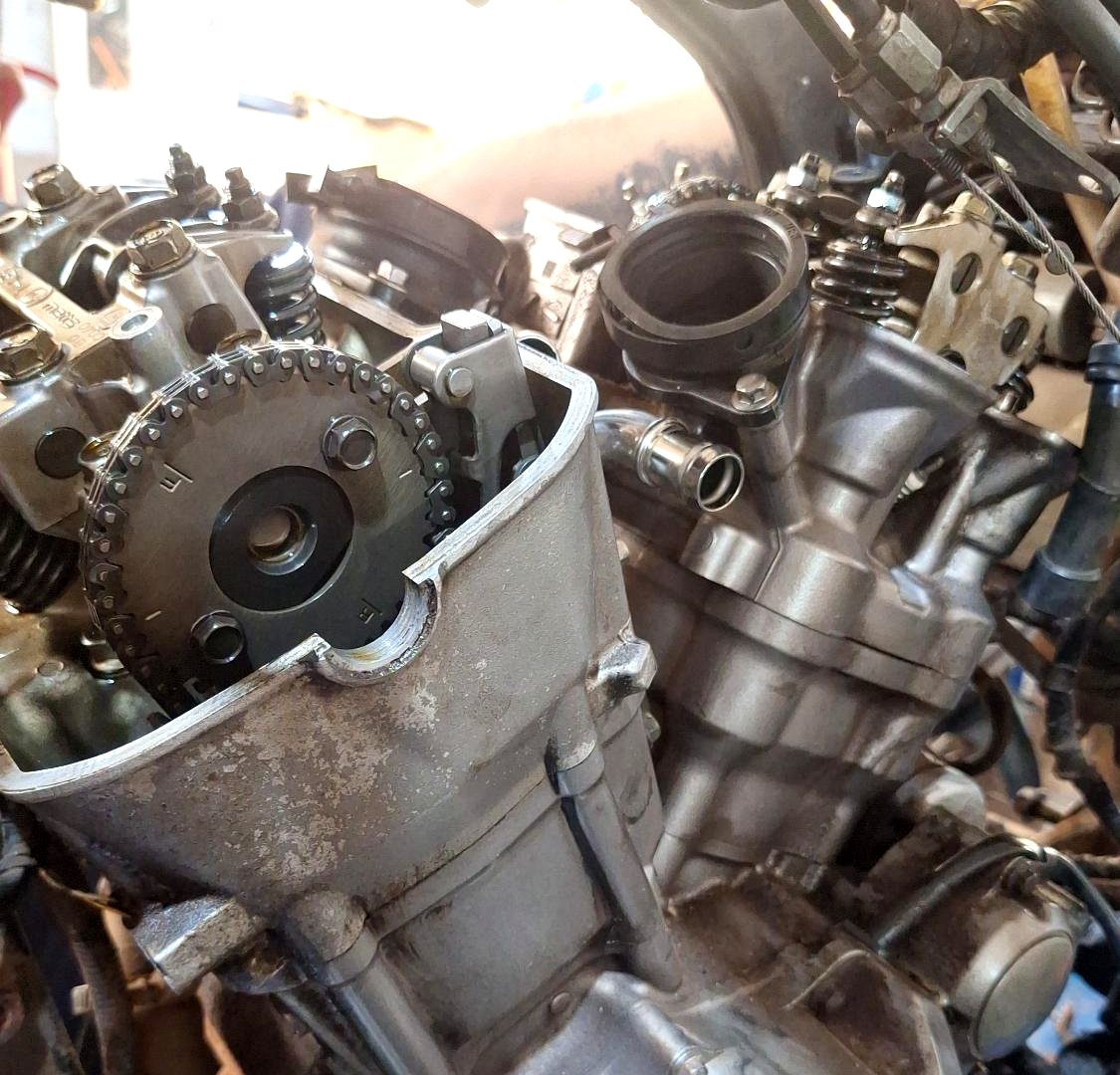 Motor de moto aberto na bancada, com o comando e a admissão à vista.